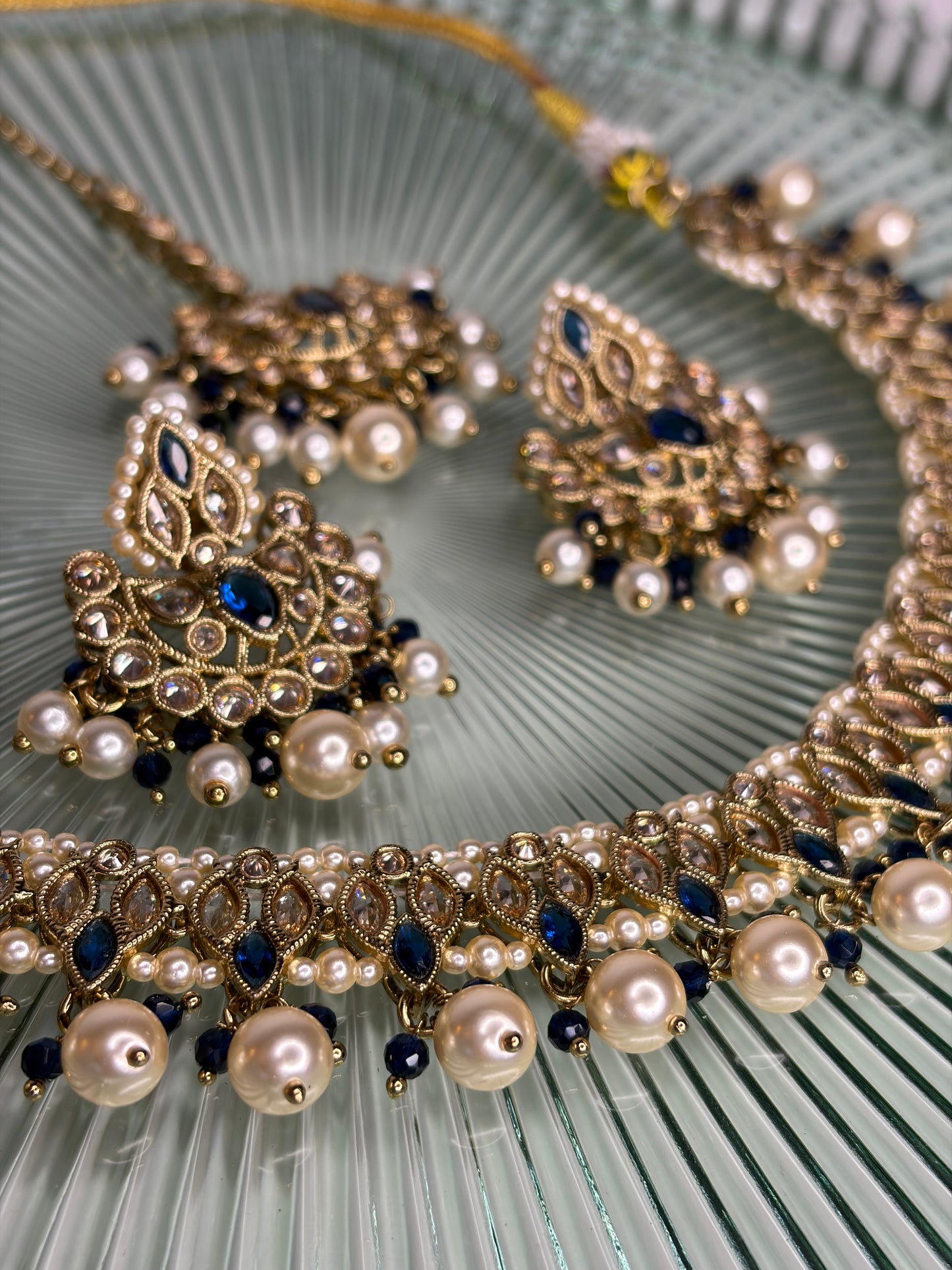 Ornate necklace with pearls and blue stones on a textured green surface