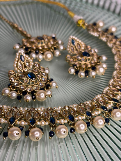 Ornate necklace with pearls and blue stones on a textured green surface